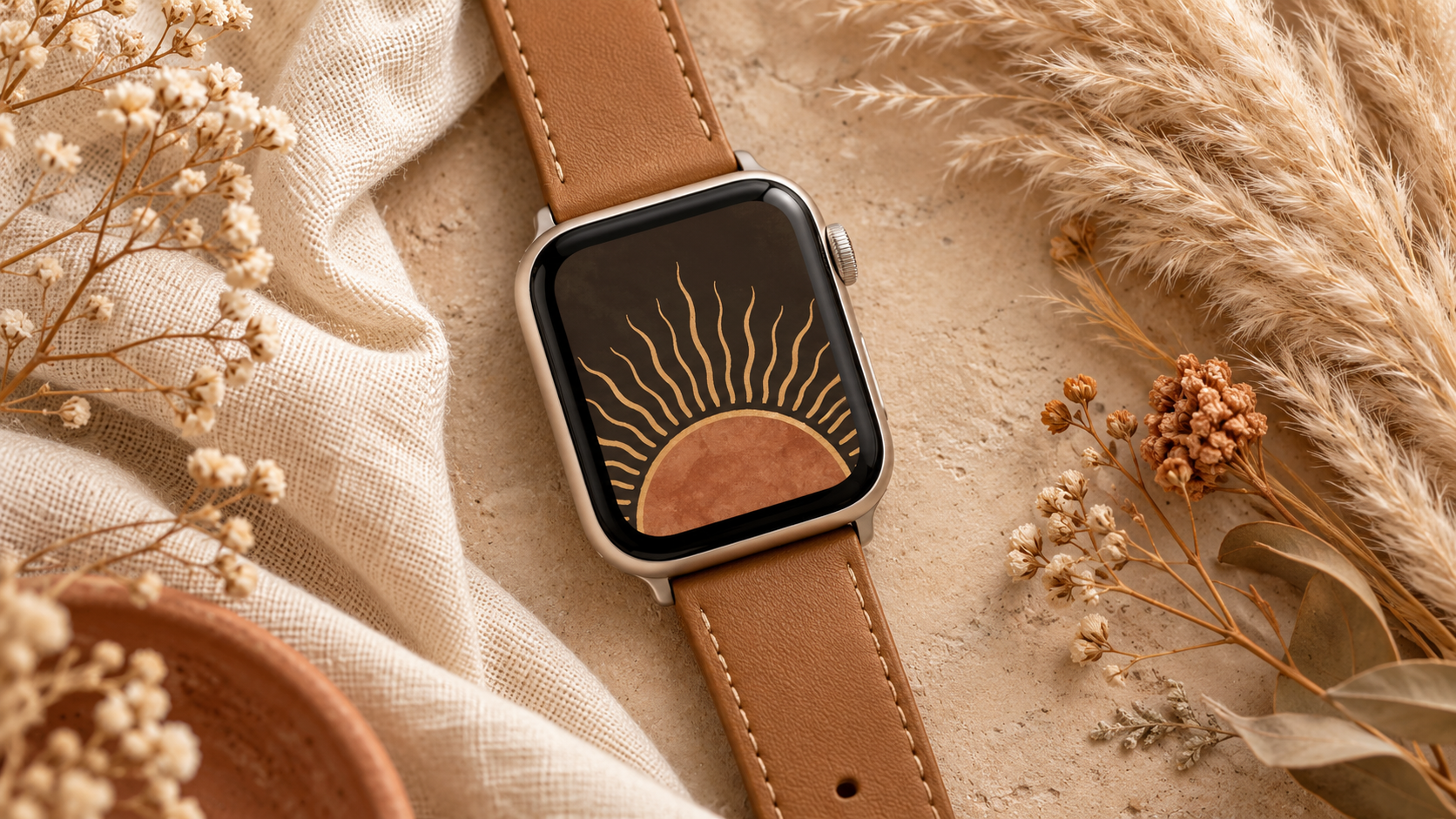 Apple Watch with boho sun arc wallpaper on tan leather band surrounded by pampas grass and dried flowers